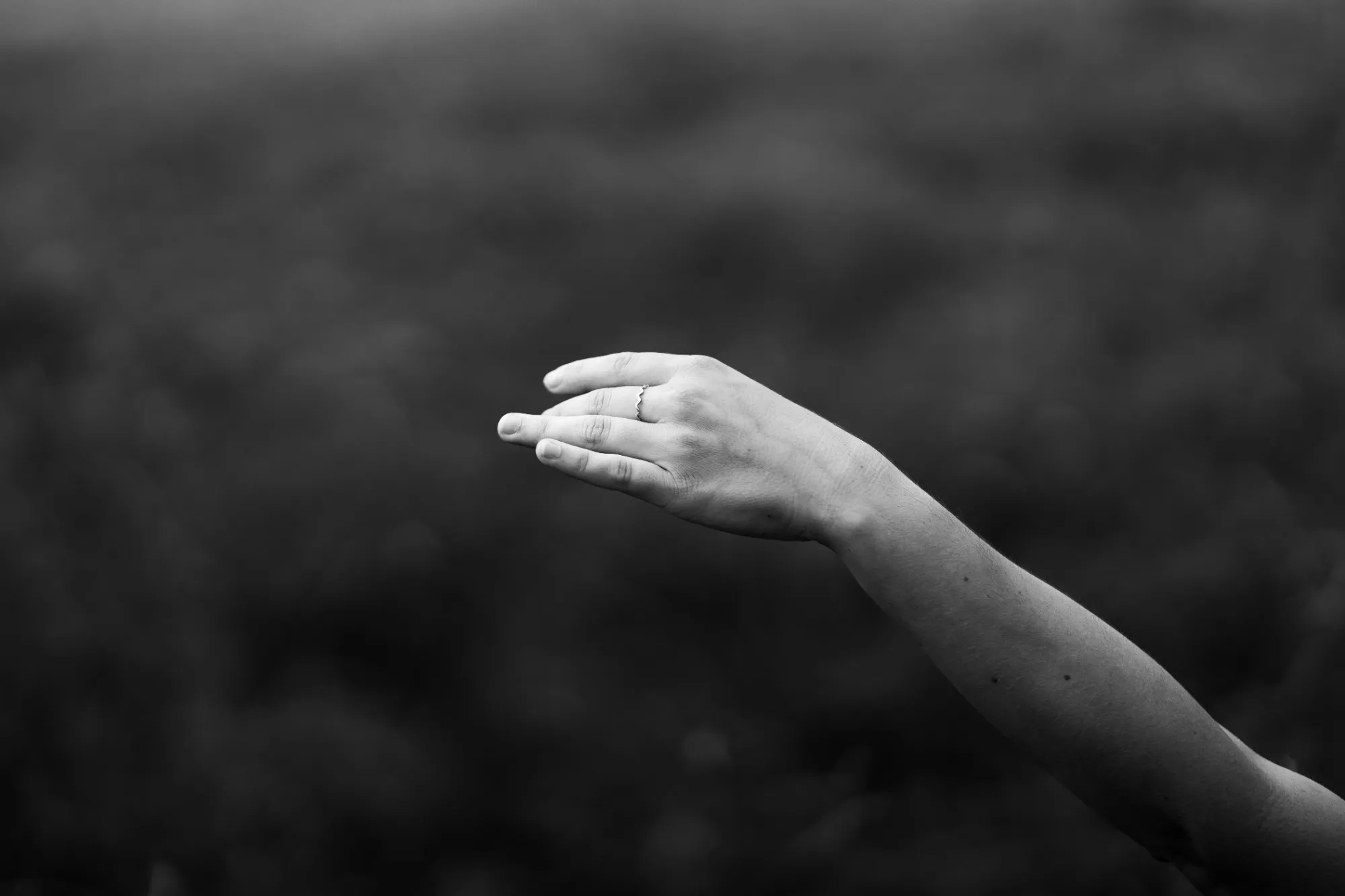 Ausgestreckter Arm mit leicht gebeugter Hand vor dunklem, unscharfem Hintergrund