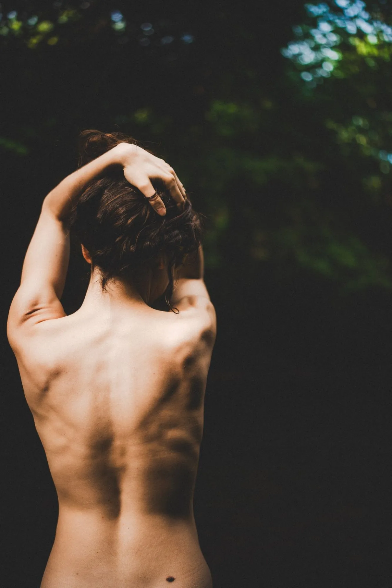 Nahaufnahme eines Rückens mit Licht und Schatten der Blätter, eine Hand im hochgesteckten Haar